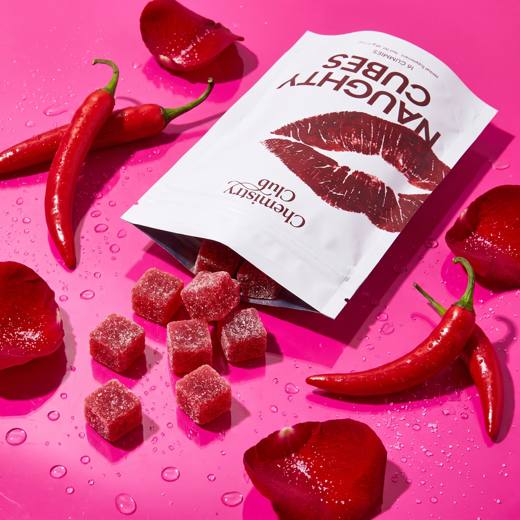 Pouch tilted on a pink surface, cubes spilling out, chili peppers and rose petals