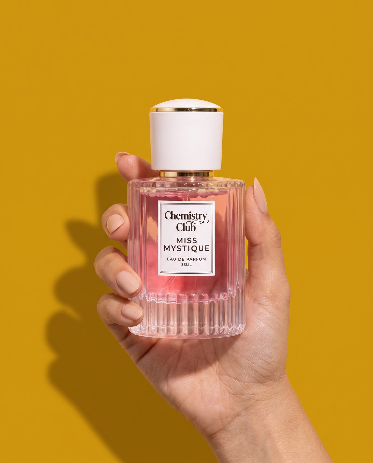 Hand holding the Miss Mystique bottle on a mustard background