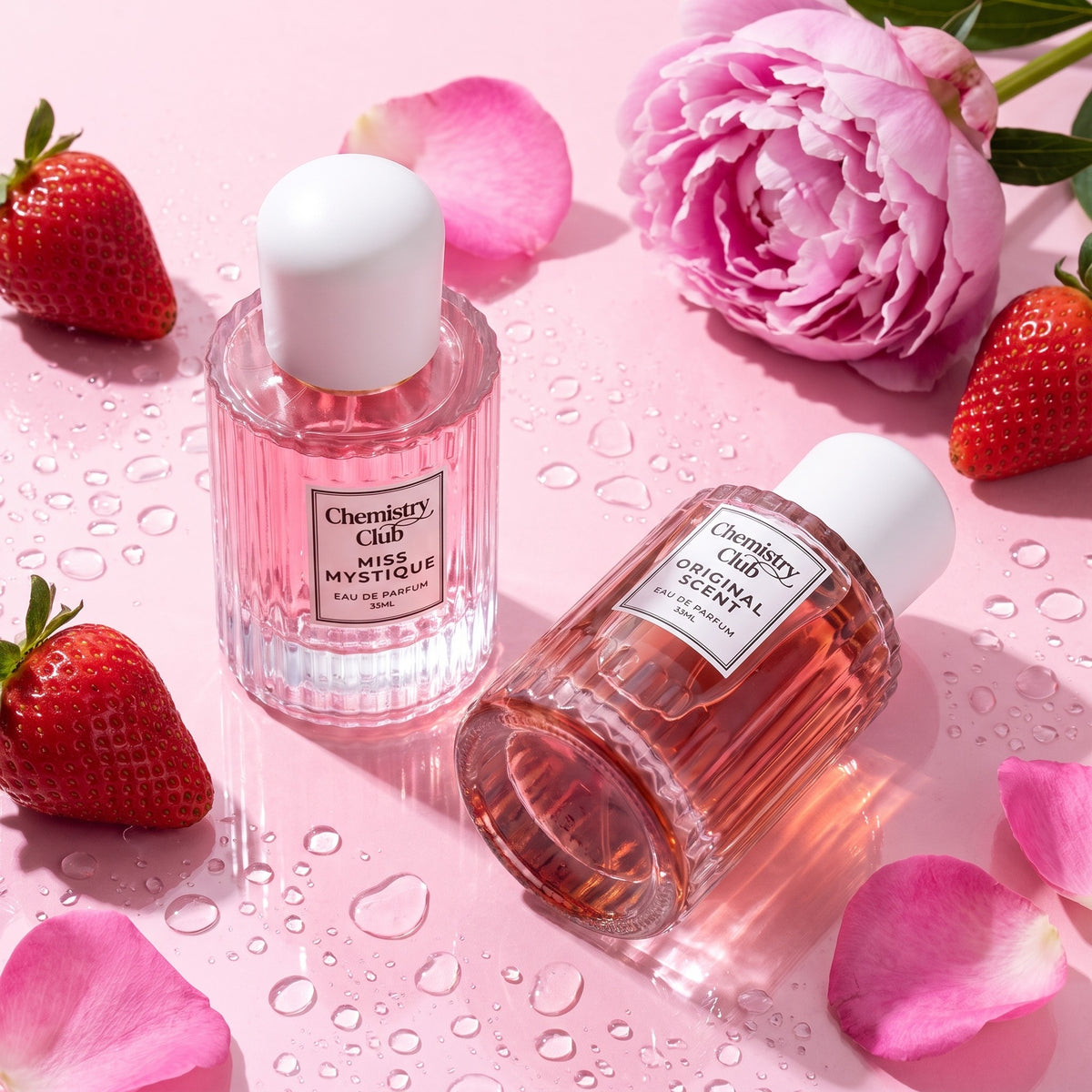 Two Chemistry Scent bottles on a glossy pink surface with strawberries, a peony and rose petals